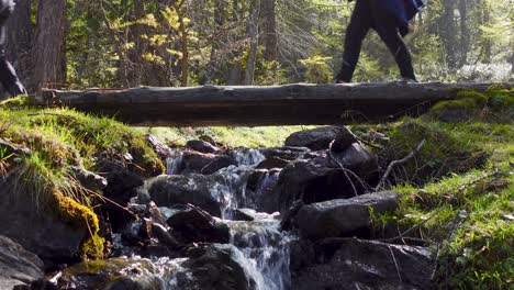 Hikers-crossing-a-wooden-bridge-over-a-small-mountain-creek-flowing-down-a-stony-stream-bed