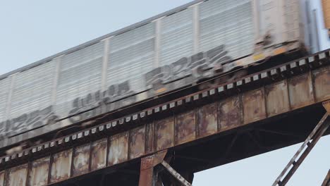 Auto-Carrier-Train-Covered-in-Graffiti-Crosses-an-Old,-Rusty-Railroad-Trestle-at-Sunset