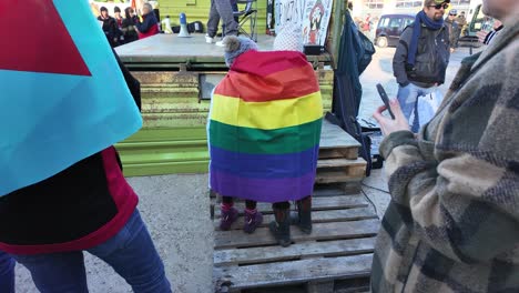 Zwei-Kinder-In-Einer-Regenbogenfahne-Kuscheln,-Während-Um-Sie-Herum-Proteste-Gegen-Die-Rechtsextremen-Stattfinden