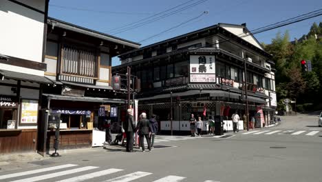 Los-Turistas-Pasan-Por-La-Intersección-En-Takayama,-Japón,-Con-Los-Coches-Recorren-Las-Avenidas-Rodeadas-De-Negocios-Y-Restaurantes.