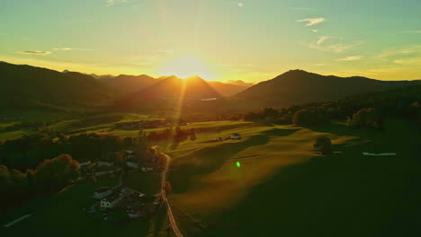Beautiful-drone-shot-of-sun-rays-over-a-mountain-in-a-green-field-surrounded-by-nature-and-trees