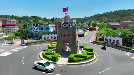 Aerial-approaching-shot-of-tourist-on-historic-tower-at-roundabout-on-Kinmen-Island-during-Sunny-day---Historic-soldier-monument-with-waving-flag