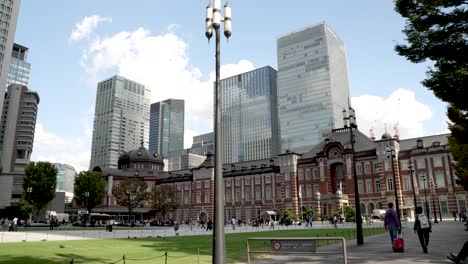 tokyo-station-surrounded-by-its-buildings,-skyscrapers-and-parks-in-the-Marunouchi-shopping-district-in-Chiyoda,-Tokyo,-Japan,-with-the-esplanade-crowded-with-people