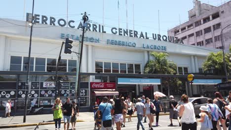 Argentine-People-Cross-the-Street-at-Chacarita-Railway-Station-Summer-Skyline,-Federico-Lacroze-Train-Station,-Ferrocarril-Urquiza-Line
