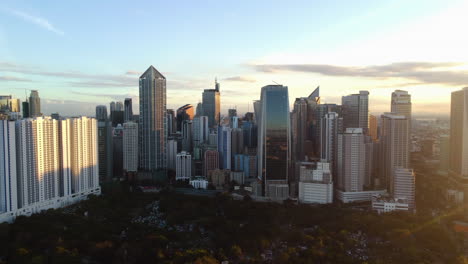Aerial-rising-shot-of-the-Manila-South-Cemetery-and-the-Makati-city-skyline,-sunset-in-the-Philippines