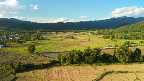 Beautiful-Small-Mountain-Village-with-Rice-Fields-after-Harvest-surrounded-by-Mountains,-Mueang-Khong-Northern-Thailand-Remote-Farming-and-Agriculture-Land,-Aerial-View