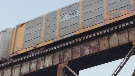 Un-Tren-De-Transporte-De-Automóviles-Cubierto-De-Graffiti-Cruza-Un-Viejo-Y-Oxidado-Caballete-De-Ferrocarril-Al-Atardecer