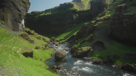 Cascada-De-Kvernufoss-Y-El-Río-Abajo-En-Islandia,-Rocas-Verdes-Soleadas-Y-Agua-Corriendo-En-Primer-Plano