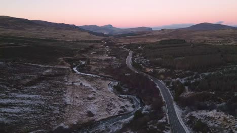Winding-road-through-a-rugged-landscape-at-dusk,-Skye,-aerial-view