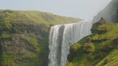 Majestic-Skogafoss-waterfall-in-Iceland,-beautiful-sunny-day-with-birds-flying-above-the-mossy-cliffs-and-rocks