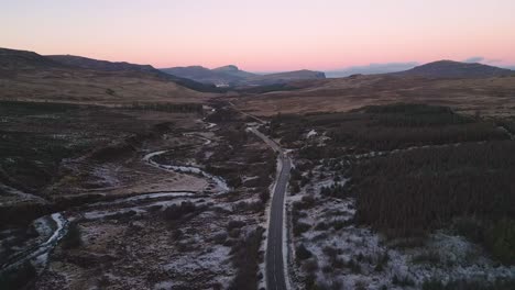 Winding-road-through-a-rugged-landscape-at-dusk,-light-snow-cover,-Skye
