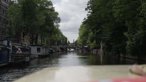Riding-on-a-boat-through-Amsterdam-canal-showing-the-green-cityscape-with-a-lot-of-trees-and-as-a-traditional-way-of-transportation