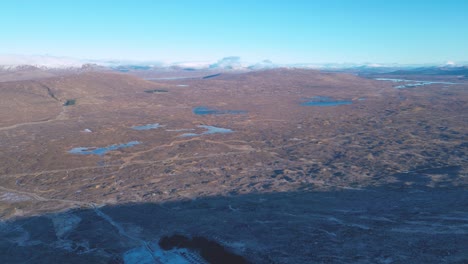Rugged-landscape-of-Skye-with-scattered-lochs,-under-a-clear-blue-sky,-aerial-view