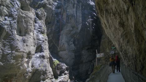 Escaladores-Caminando-Por-El-Sendero-En-Una-Pintoresca-Cueva-Abierta-|-Cueva-De-Grindelwald-Suiza-En-El-Cañón-Del-Glaciar,-Europa,-4k