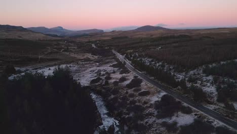 Snowy-landscape-at-dusk-with-road-winding-through,-Skye,-aerial-view