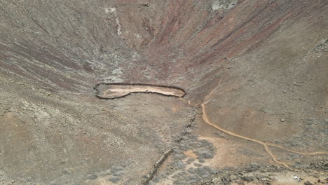 Aerial-view-rising-above-Volcanes-de-Bayuyo-crater,-Fuerteventura-rocky-volcanic-basin-interior