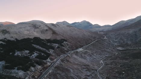 Winding-road-through-the-snowy-landscape-of-Skye-at-dawn,-aerial-view