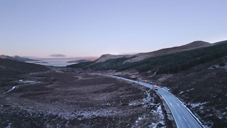 Lone-vehicle-driving-through-a-rugged-landscape-on-the-Isle-of-Skye-at-dusk,-winter-season,-aerial-view