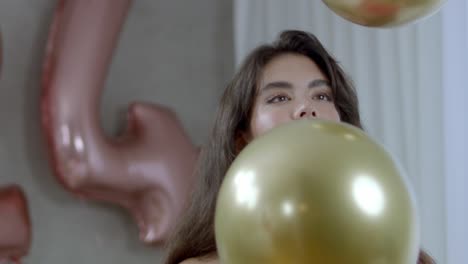 Ein-Weibliches-Model,-Das-Mit-Einem-Breiten-Lächeln-Hüpfende-Goldene-Luftballons-Betrachtet