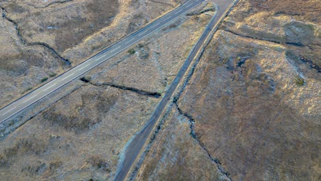 Barren-landscape-with-a-single-road-cutting-through,-Glencoe-area,-golden-hour,-aerial-view