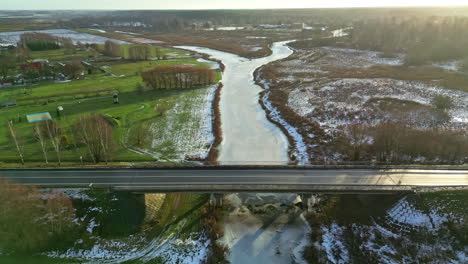 Coche-Conduciendo-Sobre-Un-Puente-Sobre-Un-Río-Congelado-Durante-El-Amanecer-En-Letonia