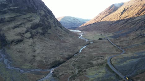 Meandering-river-through-a-valley-in-Skye-with-roads-and-hills-at-dusk,-aerial-view