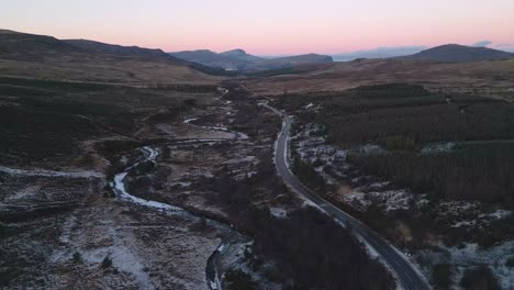 Twilight-hues-over-the-Isle-of-Skye-with-a-winding-road-and-frosted-landscape,-aerial-view