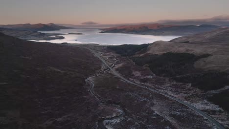 Rugged-Isle-of-Skye-landscape-at-dusk-with-winding-roads-and-serene-sea-loch,-aerial-view