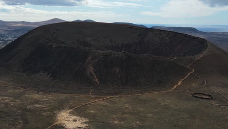 Aerial-view-rising-over-Calderón-Hondo-Volcano-crater-to-reveal-rugged-Fuerteventura-mountain-landscape
