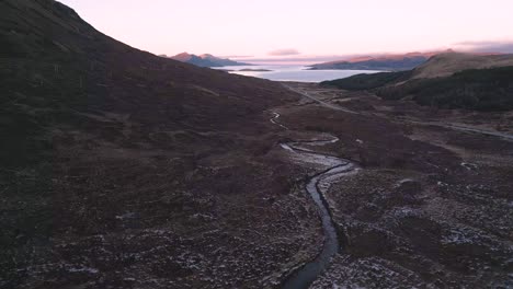 Rugged-terrain-on-the-Isle-of-Skye-during-dusk,-highlighting-winding-streams-and-distant-mountains,-aerial-view