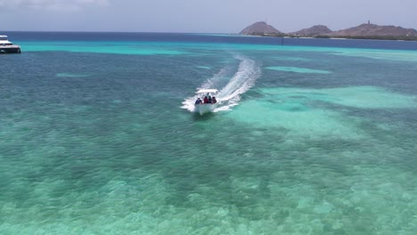 Speedboat-cruising-on-the-clear-blue-waters-of-Los-Roques,-Venezuela-with-scenic-hills-in-the-background,-daylight