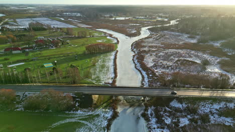 Aerial-view-of-traffic-driving-over-a-bridge-over-a-frozen-river-during-sunrise