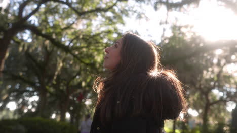 Portrait-of-beautiful-young-hispanic-woman-looking-up-at-the-trees-in-the-park-outside-on-a-sunny-afternoon,-latina,-back-lit,-proud,-nature,-surroundings,-fresh-air,-healthy,-vitality