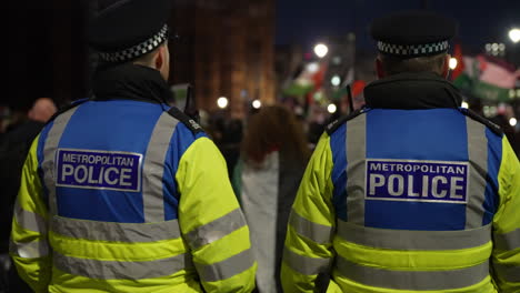 In-slow-motion-two-Metropolitan-public-order-intelligence-police-officers-stand-watching-and-monitoring-a-nighttime-protest-outside-Westminster-Abbey
