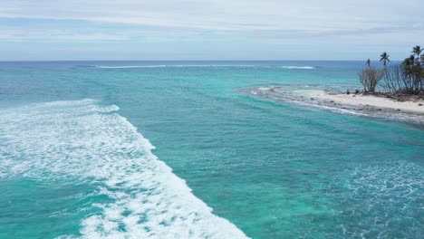 Drone-Shot-of-Turquoise-Sea-Waves-Breaking-on-Coast-of-Small-Tropical-Island-With-White-Sand