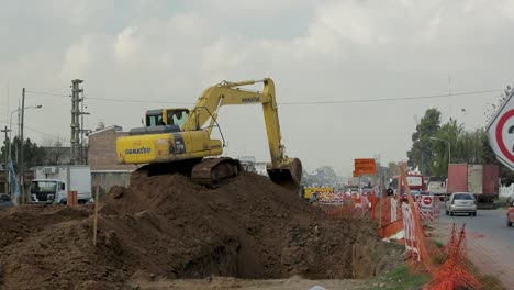 Excavator-sits-on-pile-of-dirt-pivoting-to-remove-earth-at-construction-site-in-middle-of-road