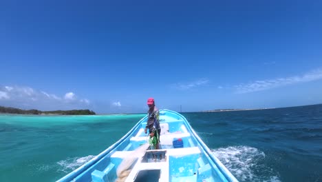 Man-standing-on-boat-moving-across-turquoise-waters-near-Los-Roques,-Venezuela,-clear-sky