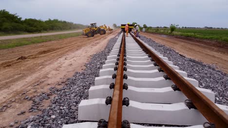 Railroad-workers-lay-sleeper,-ballast,-and-subgrade-while-fastening-rail-ties,-aerial-pullback