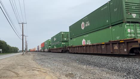 large-freight-shipping-containers-moving-fast-on-a-cargo-train-next-to-electrical-utility-structures-on-an-overcast-day