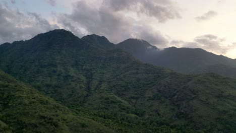 Drone-flying-over-mountains-during-sunset-covered-with-green-vegetation