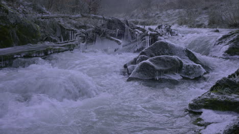Wirbelnde-Bäche-Eines-Gebirgsflusses-Im-Winter,-Vom-Fluss-Mitgebrachtes-Holz-Und-Gefrorenes,-Felsiges-Ufer