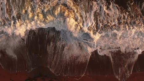 Slow-motion-aerial-view-of-waves-crashing-into-a-beach-at-sunset