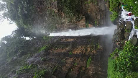 Vertical:-Tourists-explore-rugged-base-of-lush-Karas-Biru-waterfall