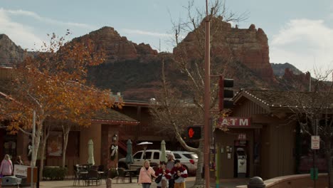 Pedestrians-and-shoppers-in-downtown-Sedona,-Arizona-with-pan-shot-down-from-red-rock-mountains-to-buildings