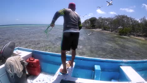 Man-fishing-from-boat-in-clear-waters-near-mangroves,-sunny-day