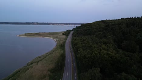 The-drone-flies-over-the-road-and-films-towards-the-Sallingsund-Bridge,-with-water-on-one-side-and-forest-on-the-other