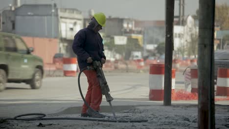 Construction-worker-uses-hydraulic-drill-at-site-as-cars-and-people-rush-by