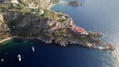 Aerial-shot-over-the-ocean-while-a-drone-orbiting-around-an-island-at-sunset-near-Taormina,-Sicily
