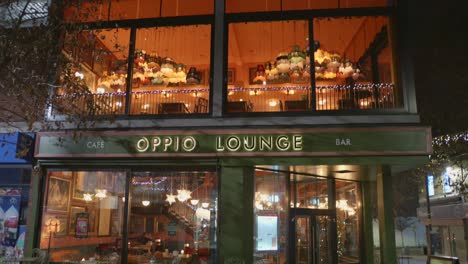 Low-angle-night-view-of-illuminated-Oppio-Lounge-Bar-beside-a-street-of-Altrincham-city-in-England