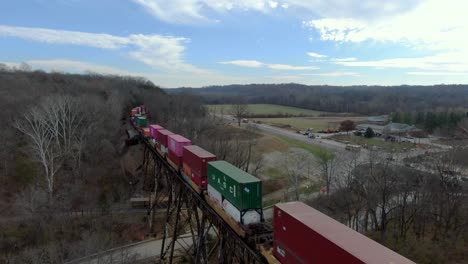 Aerial-Shot-Crossing-Over-a-Colorful-Intermodal-Train-on-the-Pope-Lick-Trestle-in-Louisville,-Kentucky-on-a-Sunny-Winter-Day